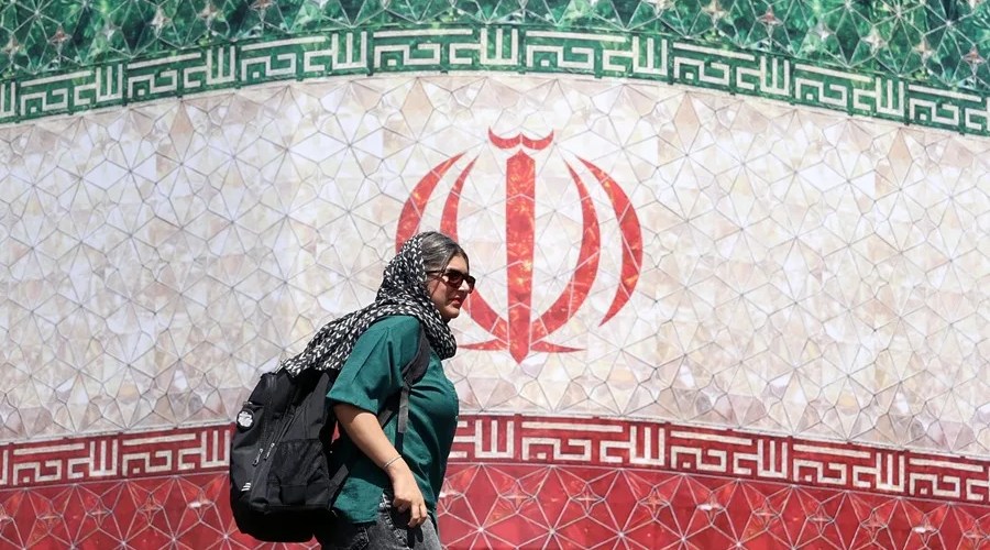Fotografía de una mujer iraní pasando junto a una valla publicitaria con la bandera de Irán en la plaza Enqelab, en Teherán (Irán). EFE/EPA/ Abedin Taherkenareh