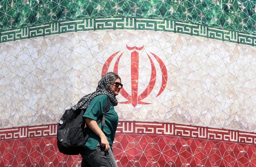 Fotografía de una mujer iraní pasando junto a una valla publicitaria con la bandera de Irán en la plaza Enqelab, en Teherán (Irán). EFE/EPA/ Abedin Taherkenareh