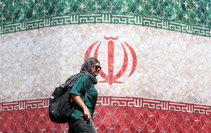 Fotografía de una mujer iraní pasando junto a una valla publicitaria con la bandera de Irán en la plaza Enqelab, en Teherán (Irán). EFE/EPA/ Abedin Taherkenareh
