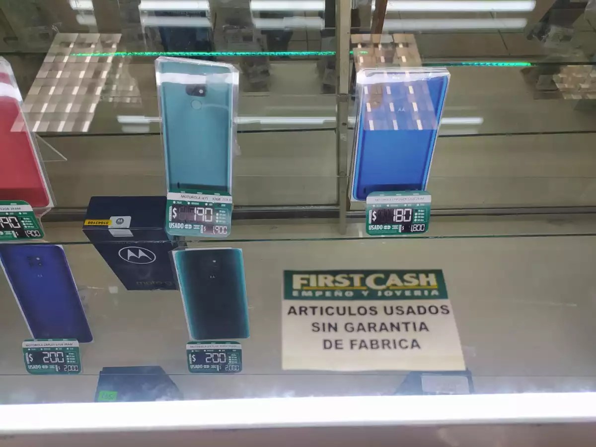 Vitrina con varios teléfonos usados de la marca Motorola en diferentes colores y precios, con un letrero que indica artículos usados sin garantía de fábrica.