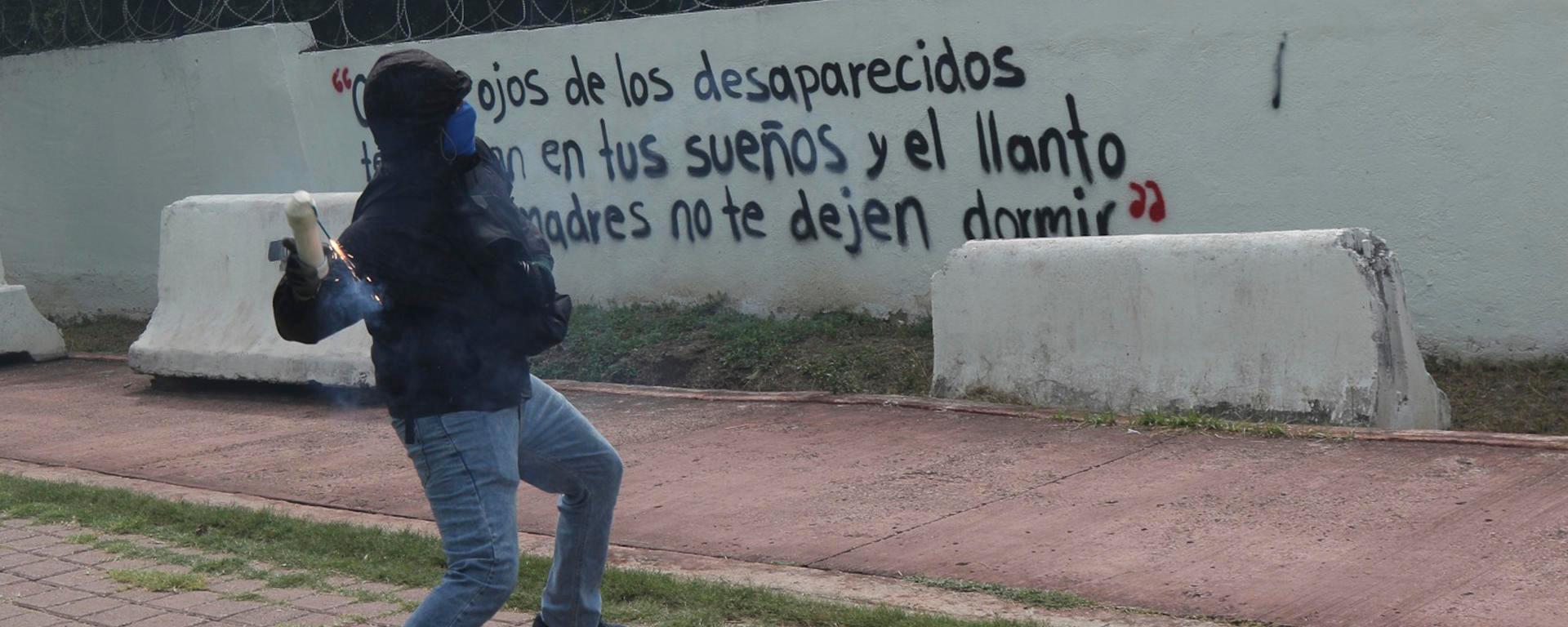 Un hombre encapuchado lanza una bomba casera al interior del 27 Batallón de Infantería, este miércoles en Iguala, Guerrero (México). Un grupo de estudiantes de la Escuela Normal Rural de Ayotzinapa lanzó bombas caseras contra instalaciones militares en Iguala (Guerrero, sur), en protesta por la falta de respuestas sobre la desaparición de los 43 normalistas, ocurrida hace casi 12 años, el 26 de septiembre de 2014. EFE/ José Luis De La Cruz