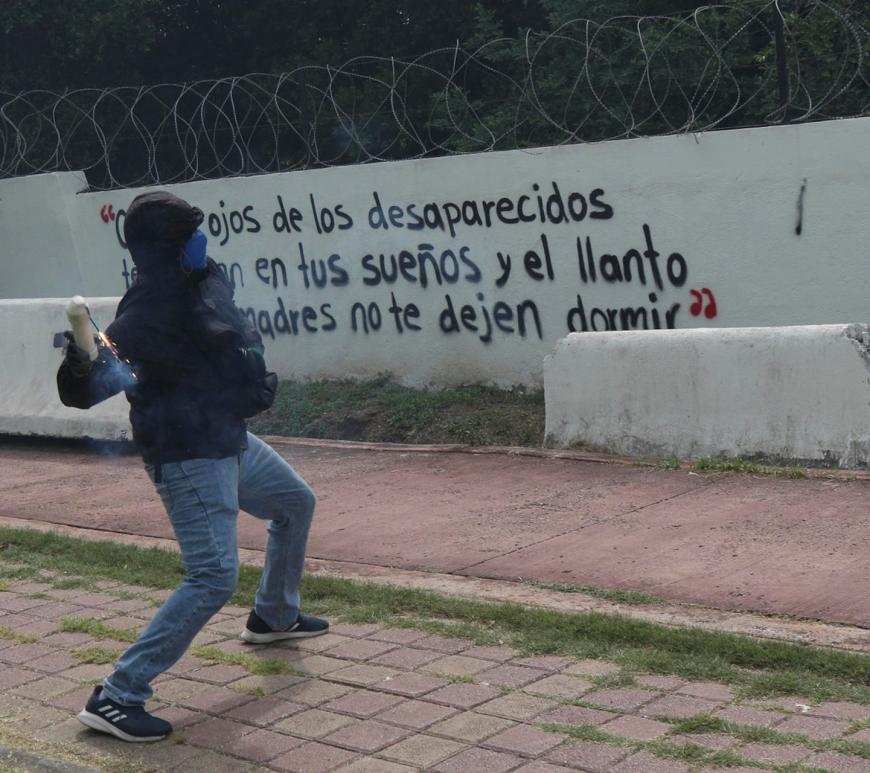 Un hombre encapuchado lanza una bomba casera al interior del 27 Batallón de Infantería, este miércoles en Iguala, Guerrero (México). Un grupo de estudiantes de la Escuela Normal Rural de Ayotzinapa lanzó bombas caseras contra instalaciones militares en Iguala (Guerrero, sur), en protesta por la falta de respuestas sobre la desaparición de los 43 normalistas, ocurrida hace casi 12 años, el 26 de septiembre de 2014. EFE/ José Luis De La Cruz