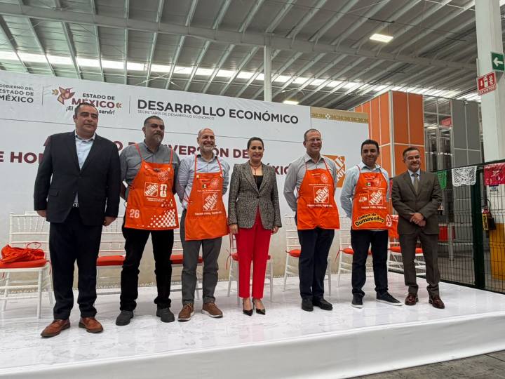 Grupo de personas posando en un evento de desarrollo económico, con una pancarta de fondo que dice 'Desarrollo Económico' y todas las personas usando delantales de Home Depot.