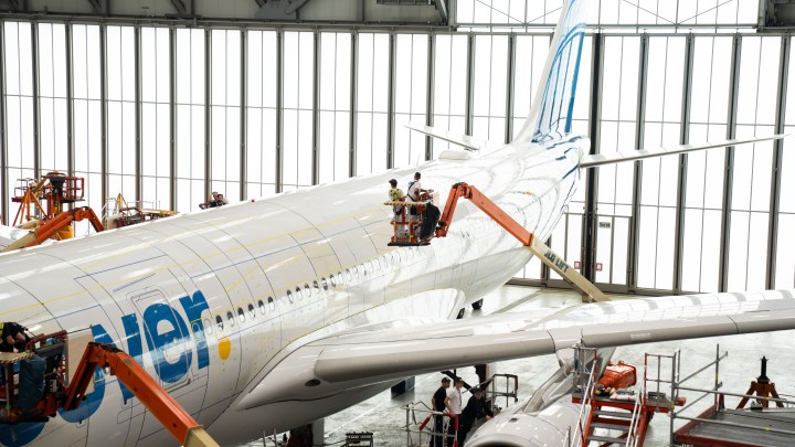 Trabajadores realizan mantenimiento en un avión dentro de un hangar, utilizando grúas elevadoras.